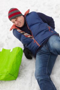 A man wearing a knitted hat lies on the floor in pain after slipping on snow