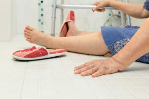 An injured person lying on the floor with one slipper having fallen off their left foot.
