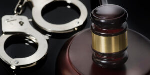Steel handcuffs and a black and brass gavel on a desk.