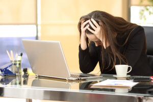 A stressed woman with her head in her hands looking at a laptop