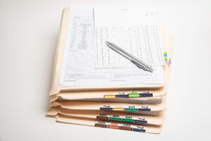 Colour-coded patient records sit in a pile on a white desk.