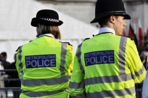 A pair of standing Metropolitan Police officers in hi-vis duty uniforms.