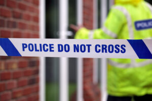 Police tape and a police officer knocking on a door after a crime of violence has occurred, resulting in multiple severe injuries