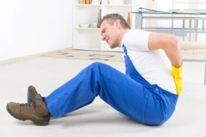 A construction worker sitting on the floor holding his back after an accident happened