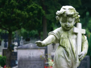 A cherub statue holding a cross in a graveyard.