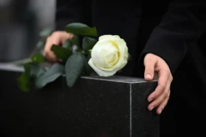 A woman placing a single white rose on a headstone.